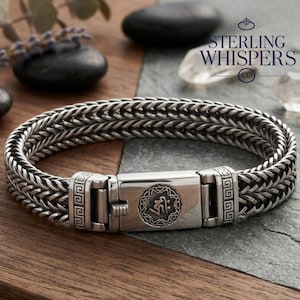 Puede incluir: Una pulsera plateada con un diseño de cadena trenzada. La pulsera presenta un cierre rectangular con un emblema grabado y patrones geométricos. La marca "STERLING WHISPERS CO" es visible en el fondo.