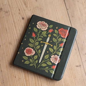 May include: Dark green metal box with a floral and sword design. The box features pink and red roses, green leaves, and a white sword with a gold hilt. Small gold stars are scattered around the design.
