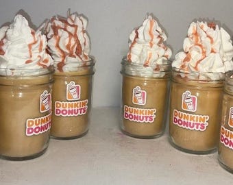 Könnte beinhalten: Sechs nach Kaffee duftende Kerzen in Gläsern, jeweils mit einem Dunkin' Donuts-Logo. Die Kerzen sind mit weißem Wachs-Schlagsahne und rot-orangem Guss bedeckt. Die Gläser sind in einer Reihe angeordnet.