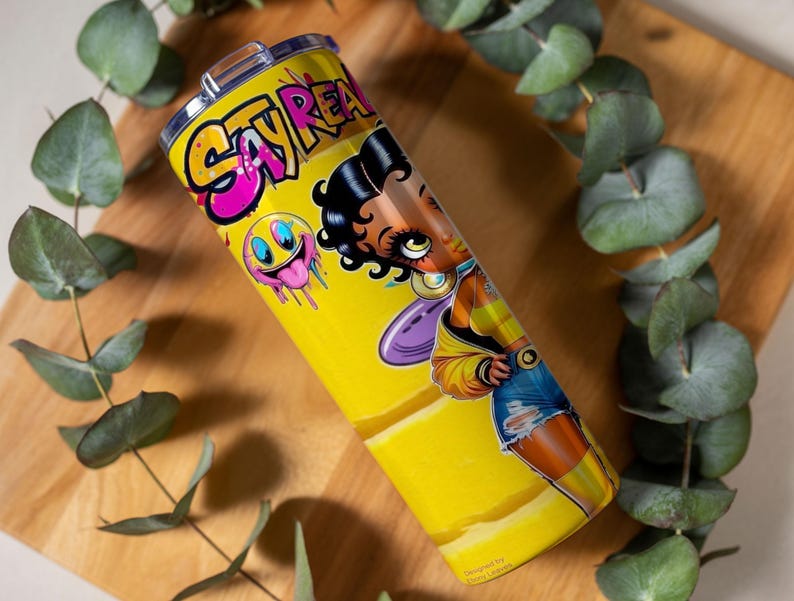 Puede incluir: Un vaso amarillo con una ilustraci&oacute;n de dibujos animados de una mujer y las palabras "Stay Real" en rosa y amarillo. El vaso tambi&eacute;n presenta una carita sonriente con baba rosa goteando. El dise&ntilde;o est&aacute; impreso en un vaso de acero inoxidable.