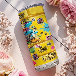 Puede incluir: Un vaso de acero inoxidable amarillo con un dise&ntilde;o de graffiti colorido. El vaso presenta las palabras "Nope Not Today" y otros grafitis. El dise&ntilde;o incluye personajes de dibujos animados, huellas de patas y un icono de c&aacute;mara.