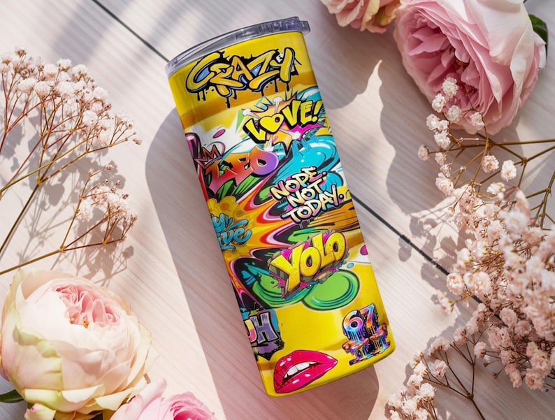 Puede incluir: Un vaso de acero inoxidable amarillo con un dise&ntilde;o de estilo grafiti. El vaso presenta las palabras "Crazy", "Love", "Nope Not Today" y "Yolo" en varios colores. Tambi&eacute;n presenta un par de labios rojos.