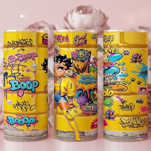 Puede incluir: Tres vasos amarillos con arte de graffiti con el personaje Betty Boop. Los vasos tienen un fondo amarillo con graffiti colorido, incluyendo la palabra "Boop" y otras frases. El dise&ntilde;o incluye im&aacute;genes de dibujos animados y colores vibrantes.