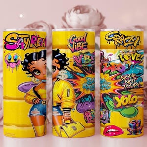 Puede incluir: Tres vasos amarillos con arte estilo grafiti. Cada vaso presenta un dise&ntilde;o diferente, incluyendo una mujer de dibujos animados, las palabras "Say Real", "Good Vibe" y "Crazy", junto con otros gr&aacute;ficos coloridos. Los vasos son cil&iacute;ndricos.