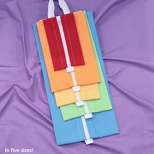Op de afbeelding: Een stapel van vijf kleurrijke, uitvouwbare pouches in rood, oranje, geel, groen en blauw, met witte ritsen en handvatten. De tekst "The Expandable Pouches" staat bovenaan, en de maatdetails staan hieronder. Op een paarse achtergrond.
