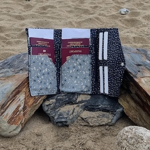 May include: A black passport folio with white polka dots and a gray floral fabric lining. The folio is open and has two passport slots, two card slots, and a cash pocket. The finished size is 8 3/4 inches by 5 inches by 3/4 inches (21 cm x 12.7 cm x 2 cm).