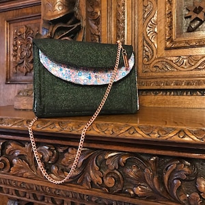 May include: A dark green glitter clutch purse with a rose gold chain strap. The flap of the purse has a white fabric lining with a colorful polka dot pattern.