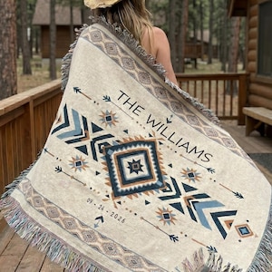 Puede incluir: Manta tejida de color crema con un diseño geométrico en tonos azules, marrones y beige. La manta presenta el texto "THE WILLIAMS" y la fecha "09.24.2026". La manta tiene un borde con flecos.