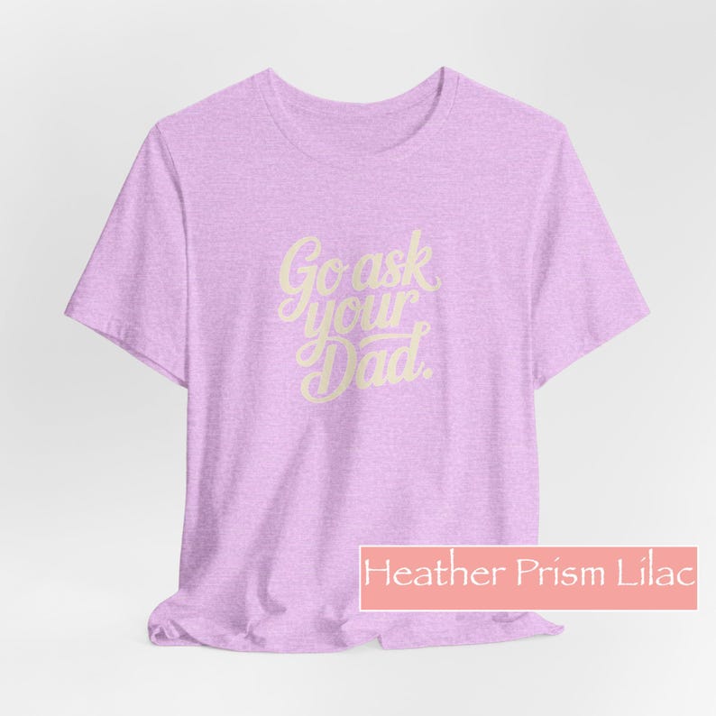 May include: A lilac t-shirt with the text "Go ask your Dad" in a cursive font. The shirt is a light purple colour and has a crew neck. The label at the bottom says "Heather Prism Lilac".