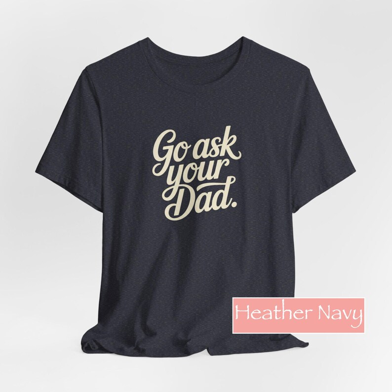 May include: Dark navy t-shirt featuring the phrase "Go ask your Dad" in a cursive font. The shirt has a crew neck and is a heathered fabric. The text "Heather Navy" is in a pink rectangle at the bottom.