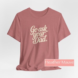 May include: Mauve heather t-shirt featuring the text "Go ask your Dad" in a cursive font. The short-sleeved shirt is a solid colour. The text is in a light beige colour.
