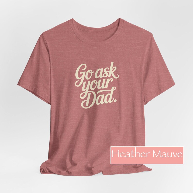 May include: Mauve heather t-shirt featuring the text "Go ask your Dad" in a cursive font. The short-sleeved shirt is a solid colour. The text is in a light beige colour.