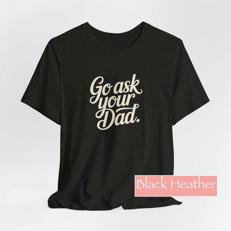 May include: Black heather t-shirt featuring the phrase "Go ask your Dad" in a cursive font. The shirt has a crew neck and short sleeves. The text is in a light beige colour, suitable for everyday wear.