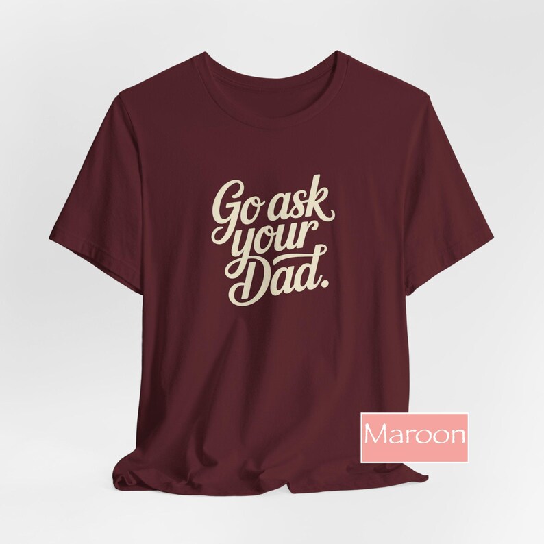 May include: Maroon t-shirt with the text "Go ask your Dad" in a cursive font. The shirt is a solid maroon colour and has short sleeves. The word "Maroon" is in a pink box in the bottom right corner.