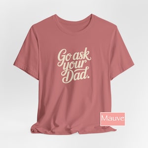 May include: Mauve t-shirt featuring the text "Go ask your Dad" in a cursive font. The shirt has a crew neck and is a solid colour. The text is in a light cream colour.