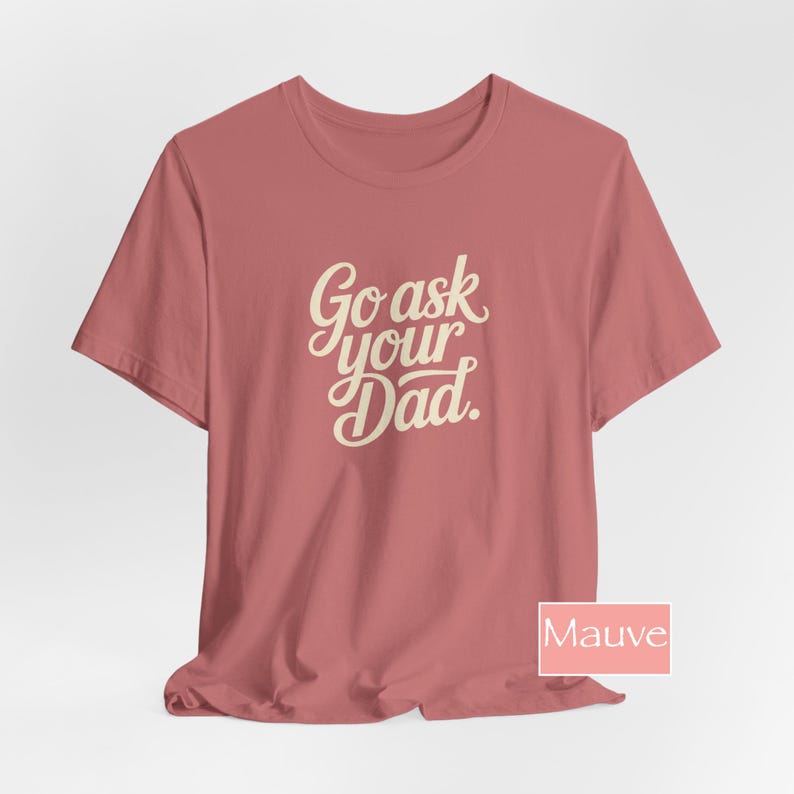 May include: Mauve t-shirt featuring the text "Go ask your Dad" in a cursive font. The shirt has a crew neck and is a solid colour. The text is in a light cream colour.