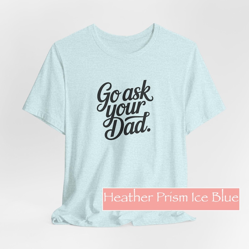 May include: Pale blue t-shirt featuring the phrase "Go ask your Dad" in black script. The shirt is a Heather Prism Ice Blue colour. A casual tee for everyday wear.