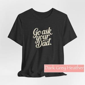 May include: Dark grey heather t-shirt featuring the text "Go ask your Dad" in a cursive font. The shirt has a crew neck and short sleeves. The words "Dark Grey Heather" are in a pink rectangle at the bottom.
