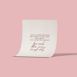 May include: A cream-colored card with the text "Love is not about how many days, months, or years you've been together. Love is about how much you love each other every single day." on a pink background.