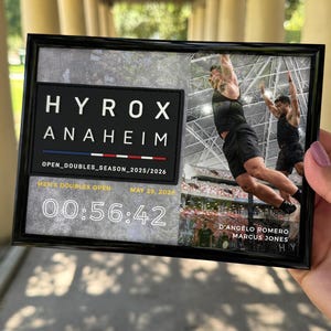 Puede incluir: Una placa conmemorativa enmarcada del evento Hyrox Anaheim Open Doubles Season 2025/2026 del 29 de mayo de 2026. Incluye el texto Hyrox Anaheim, un tiempo de 00:56:42 y una fotografía de dos atletas realizando un salto en un estadio.