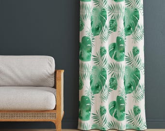 May include: A white curtain with a repeating pattern of large green monstera leaves and smaller fern-like leaves. The curtain is hanging in front of a dark blue wall, next to a light gray sofa with wooden arms.