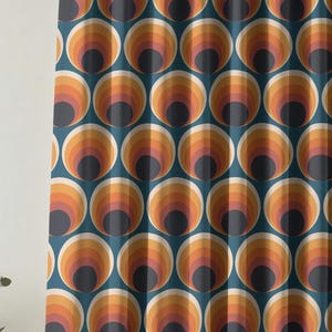 May include: A teal curtain with a repeating pattern of retro-style concentric circles. The circles feature a gradient of colours, including orange, yellow, and pink, with a dark grey centre. The curtain is hanging from a gold-coloured rod.