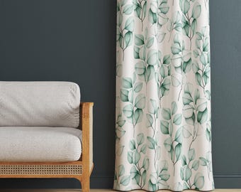May include: A white curtain with a repeating pattern of green eucalyptus leaves. The leaves have a watercolor effect. The curtain is hanging in front of a dark blue wall. A light gray sofa with wooden arms is to the left.