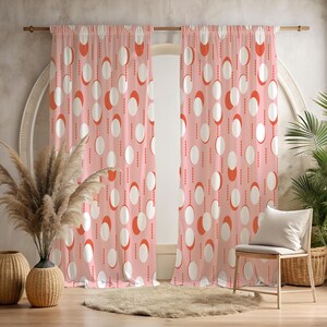May include: Pink curtains featuring a repeating pattern of white ovals and orange half-circles linked by dotted lines. The curtains are suspended from a wooden rod, framing a window. A chair with a white cushion is nearby, with decorative vases and plants.
