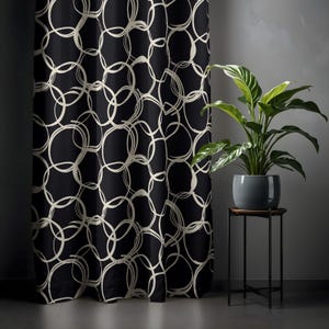 Può includere: Tenda nera con un motivo ripetuto di cerchi bianchi sporchi sovrapposti. Accanto alla tenda, una pianta in vaso con foglie verdi è posta su un piccolo supporto.