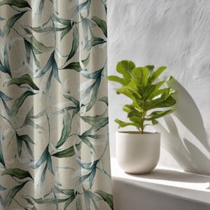 May include: Beige curtain panel with a watercolor-style leaf pattern in shades of green and blue. A potted plant with large green leaves sits on a white windowsill next to the curtain. The plant is in a white ceramic pot.