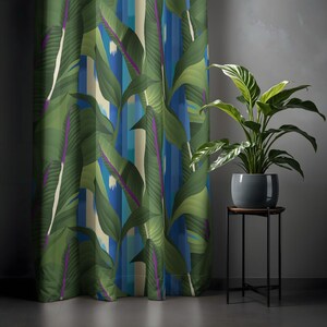 Könnte beinhalten: Vorhang mit tropischem Blattmuster in Grün- und Blautönen mit vertikalen Streifen. Der Vorhang befindet sich neben einer Topfpflanze auf einem schwarzen Metallständer. Die Blätter haben violette Akzente.