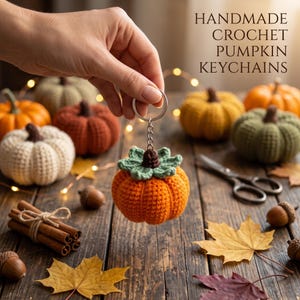 May include: A handmade crochet pumpkin keychain featuring a bright orange pumpkin with a green leaf top and a silver metal ring. The text HANDMADE CROCHET PUMPKIN KEYCHAINS is visible in the upper right corner of the image.