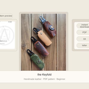 May include: Four leather key holders in shades of brown and green with black metal clasps are displayed on a wooden surface. The key holders are in various colors, including tan, dark brown, and olive green. The text "the Keyfold" is visible.