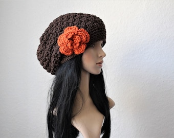 May include: A brown crochet hat with an orange flower accent. The hat is a soft, textured knit, and the flower is a vibrant, three-dimensional design. This handmade hat is a stylish accessory.