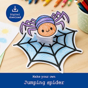 May include: A paper craft jumping spider with a purple and orange body and a light blue web base. The spider has a smiling face and is elevated on a small white paper spring. The text "Digital download" and "Make your own Jumping spider" appear.
