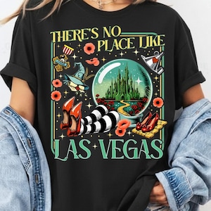May include: Black t-shirt with a colorful graphic that reads "THERE'S NO PLACE LIKE LAS VEGAS." The design includes a crystal ball with a castle, red shoes, and poppy flowers.