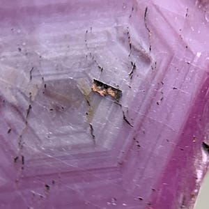 Könnte beinhalten: Ein durchscheinender rosa Edelstein mit einem deutlichen hexagonalen Wachstumsmuster auf der Oberfläche. Der Kristall weist konzentrische geometrische Linien auf, die von der Mitte ausstrahlen, durchsetzt mit dunklen, dünnen, linearen Einschlüssen.