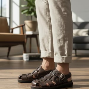 May include: A pair of dark brown leather fisherman sandals featuring a woven strap design, a closed rounded toe, and an adjustable ankle strap with a silver-toned metal buckle. The sandals have a thick, dark, flat rubber sole and a sturdy construction.