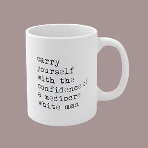 May include: White ceramic mug with a curved handle. The mug features black text that reads "carry yourself with the confidence of a mediocre white man."