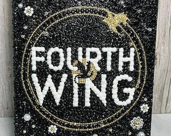 May include: A black book cover embellished with black beads, white pearls, and gold accents. The title "FOURTH WING" is prominently displayed in white, encircled by a gold design. The author's name, REBECCA YARROS, is at the bottom.