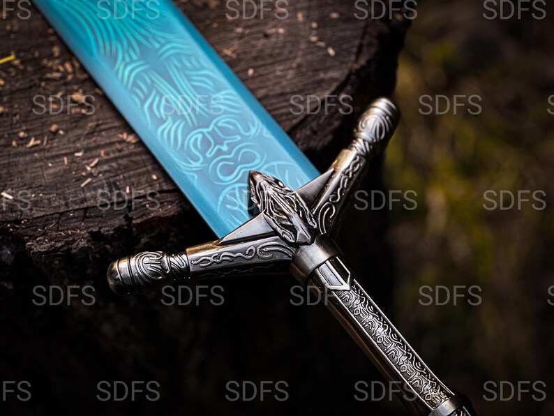 May include: A detailed image of a fantasy sword with a light blue blade featuring intricate etched designs. The hilt and crossguard are silver-toned with ornate carvings. The sword rests on a dark, textured wooden surface.