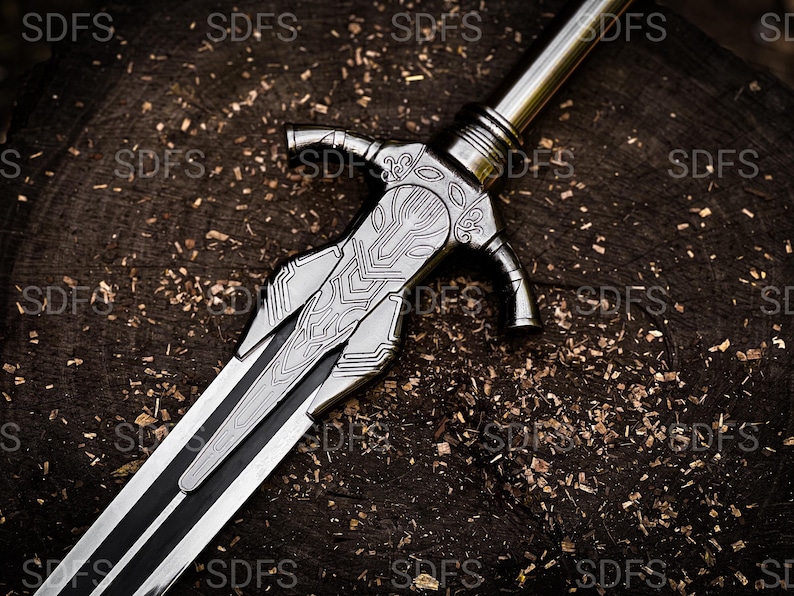 May include: A detailed, silver-colored sword with intricate designs on the hilt and blade. The sword features a black stripe down the center of the blade. The weapon rests on a dark, textured wooden surface.