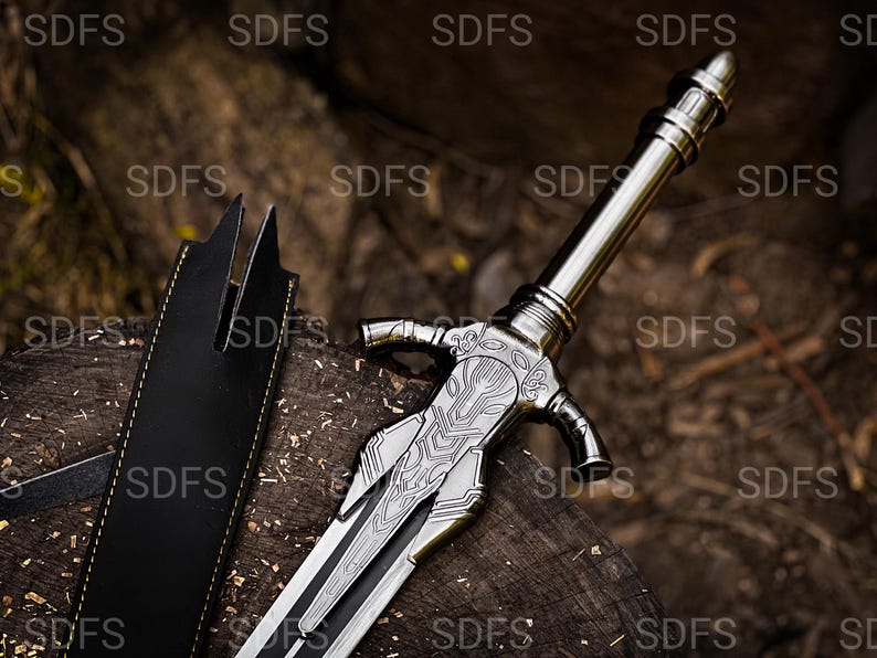 May include: A silver-colored sword with an ornate handle and blade rests on a wooden surface. A black leather sheath is positioned to the left. The sword features detailed engravings.