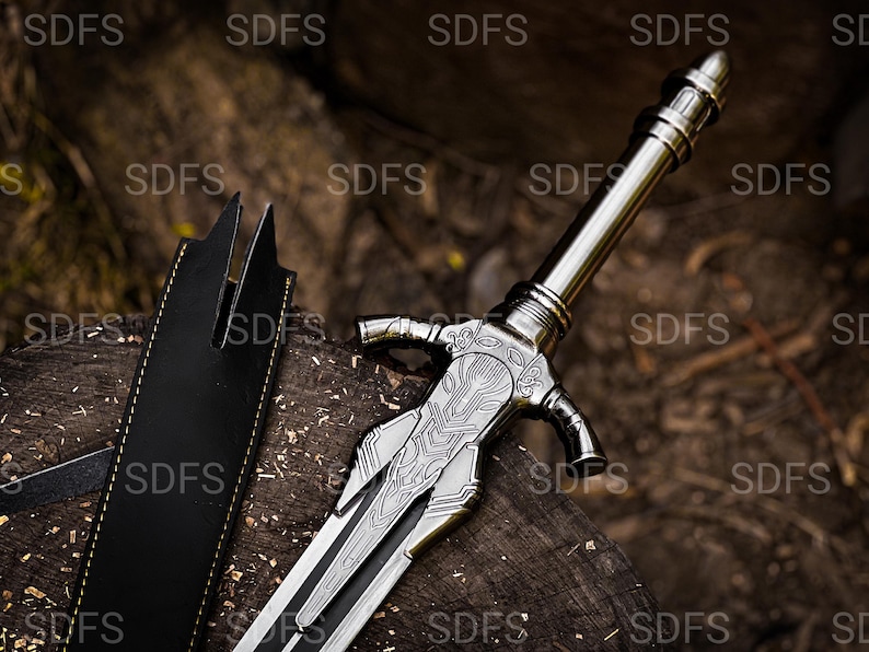 May include: A silver-colored sword with an ornate handle and blade rests on a wooden surface. The sword has a detailed design on the blade and a black leather sheath is visible to the left.