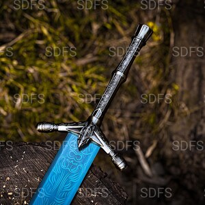 May include: A detailed sword with a blue blade and ornate silver hilt. The blade features a patterned design. The sword rests on a wooden surface, with a blurred natural background.