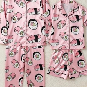 May include: Pink pajama sets with a sushi pattern. One set includes long-sleeved top and pants, the other a short-sleeved top and shorts. The sushi design features various sushi rolls in black, white, and green.