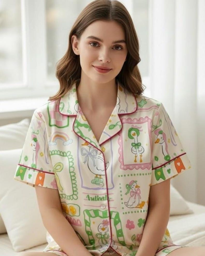 Puede incluir: Conjunto de pijama color crema con un estampado caprichoso de patos. La parte superior de manga corta y los pantalones cortos presentan un dise&ntilde;o repetido de patos en marcos, arco&iacute;ris y detalles florales, delineados en rojo y verde. El conjunto tiene un ajuste relajado.