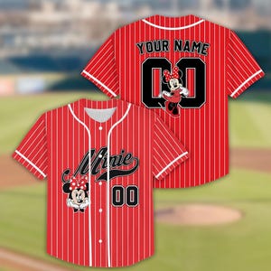 May include: Red baseball jersey with white pinstripes, featuring "Minnie" and "00" on the front, and "YOUR NAME" and "00" on the back. Minnie Mouse graphics are included. The jersey has a button-up front and white trim.