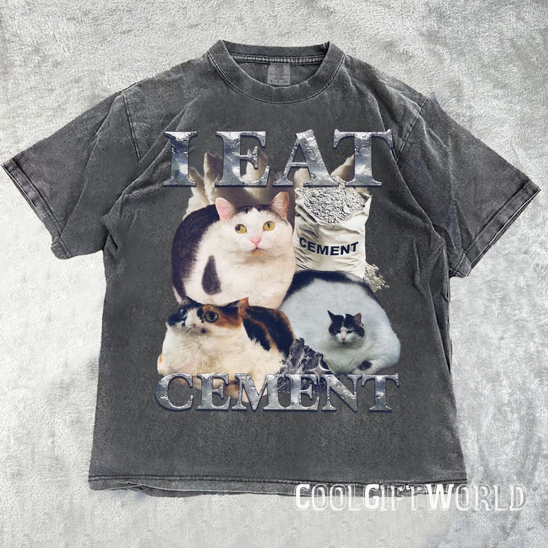 Pode incluir: Camiseta cinza escuro com um design gr&aacute;fico com quatro gatos e as palavras "I EAT CEMENT" em uma fonte met&aacute;lica. Uma saco de cimento tamb&eacute;m est&aacute; no design. A camiseta tem um visual vintage e desgastado.