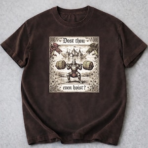 May include: Brown t-shirt with a medieval-themed illustration. The design shows a knight lifting weights, accompanied by the text "Dost thou even hoist?". The artwork includes dragons and a castle, creating a vintage aesthetic.